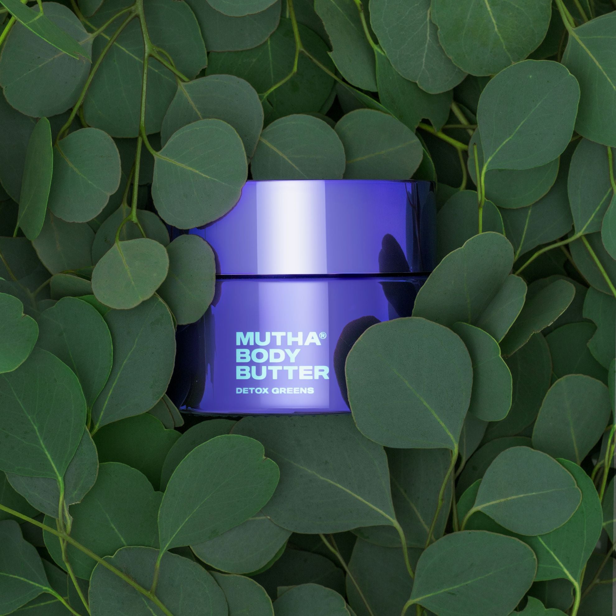 Purple jar of 'Mutha Body Butter' surrounded by green leaves