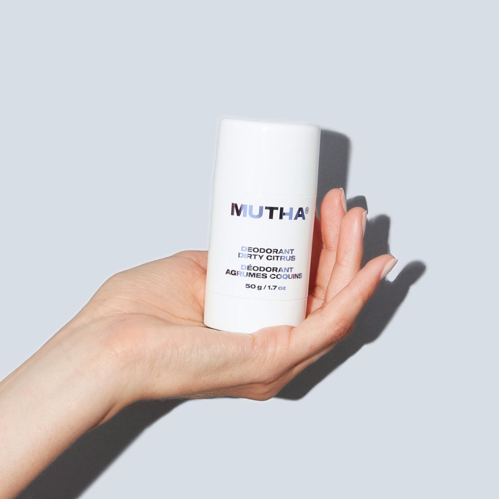Hand holding a MUTHA deodorant can against a light gray background