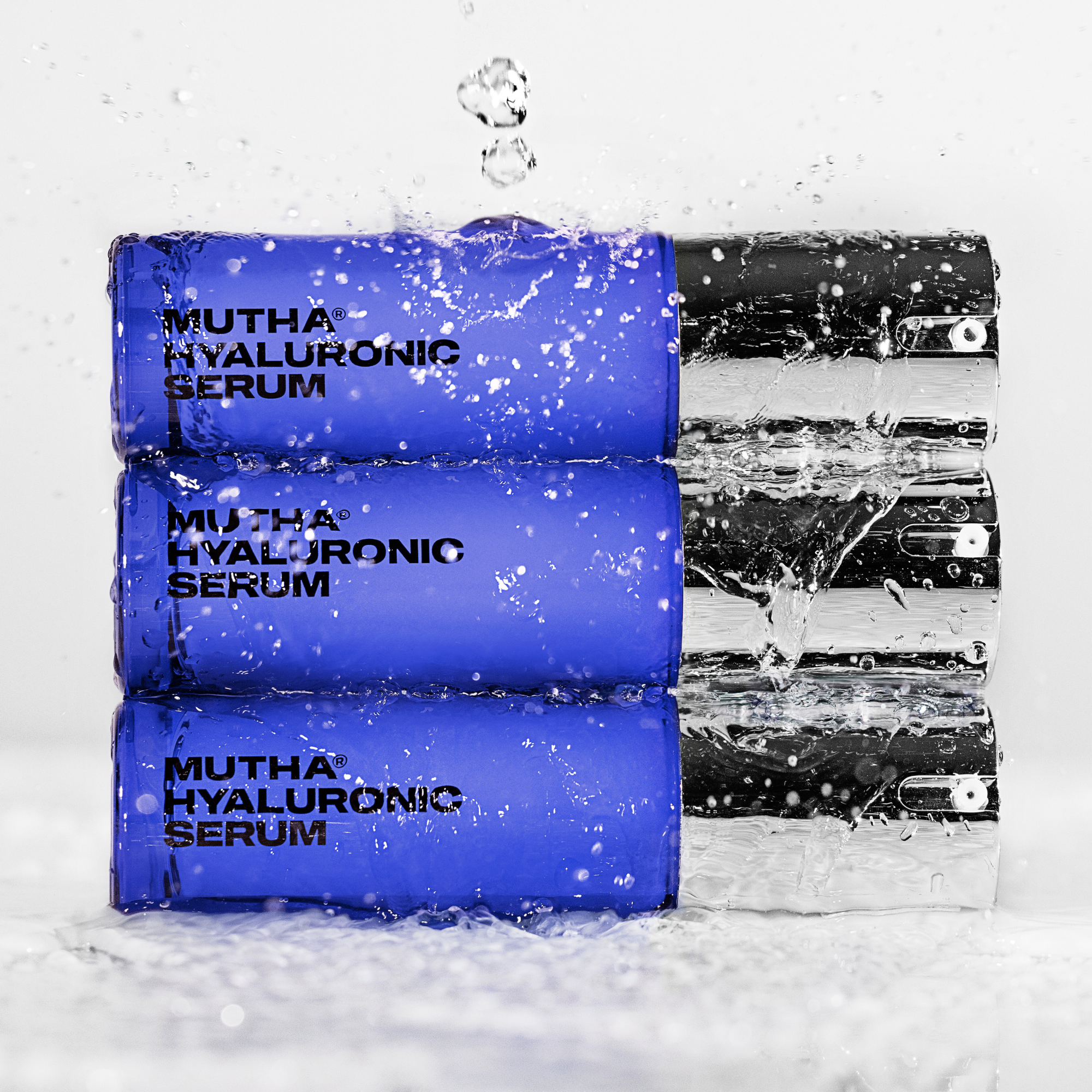 Dynamic Image of three Hyaluronic Serums stacked on top of one another with water pouring down on them and droplets in the frame