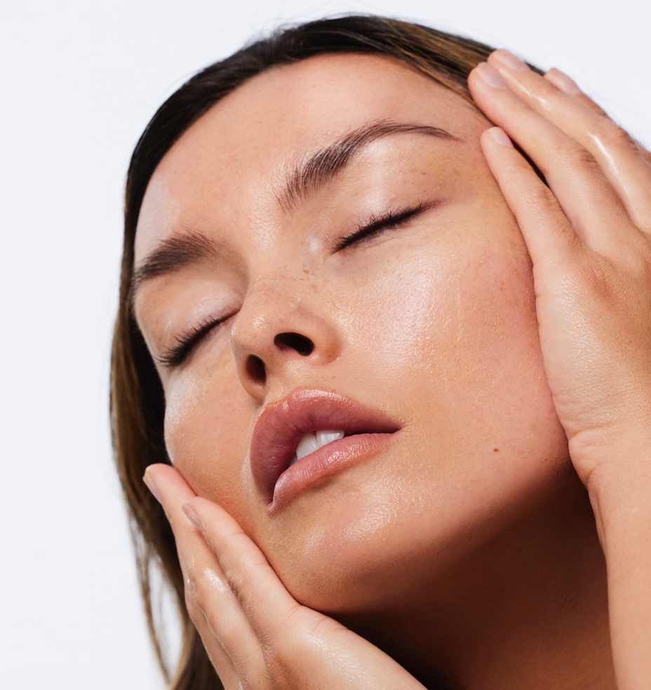 Close-up of a woman's face with hands gently touching her skin on a white background