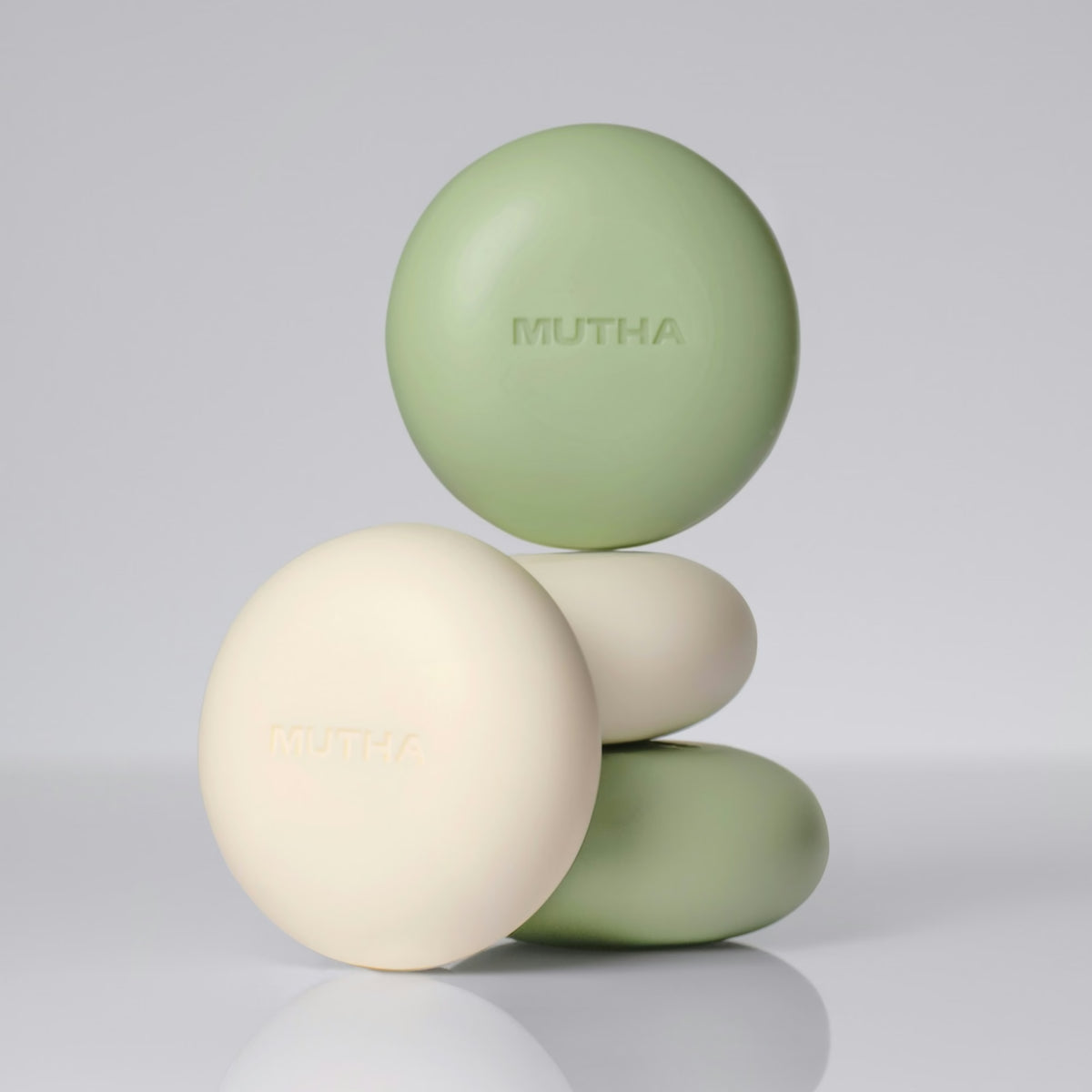 MUTHA body bars stacked in a studio shot, the green Detox Greens bar balanced above the cream Dirty Citrus bar