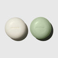 MUTHA Exfoliating Body Bars in Dirty Citrus and Detox Greens side by side on a soft grey background, each embossed with the MUTHA logo