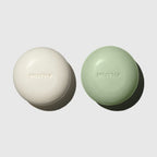 MUTHA Exfoliating Body Bars in Dirty Citrus and Detox Greens side by side on a soft grey background, each embossed with the MUTHA logo