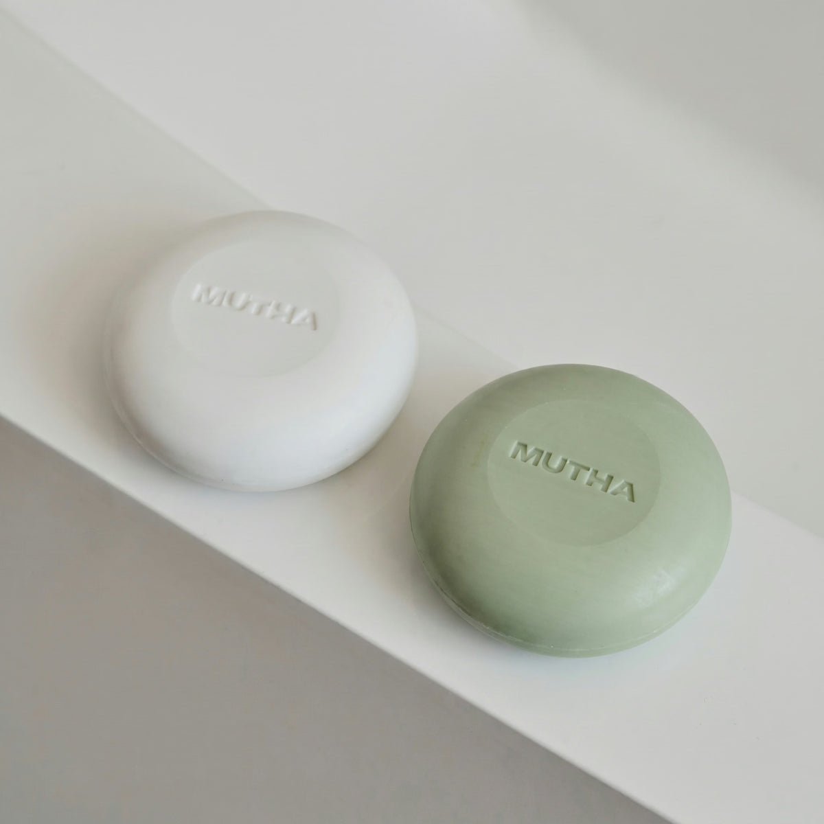 Both MUTHA body bars on a white ledge in soft daylight, the white Dirty Citrus bar beside the green Detox Greens bar