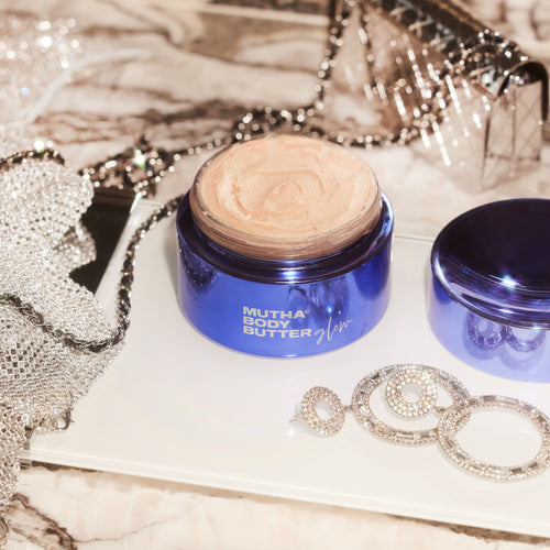 MUTHA Body Butter Glow displayed on a vanity with sparkling accessories and an open jar revealing the shimmering formula.