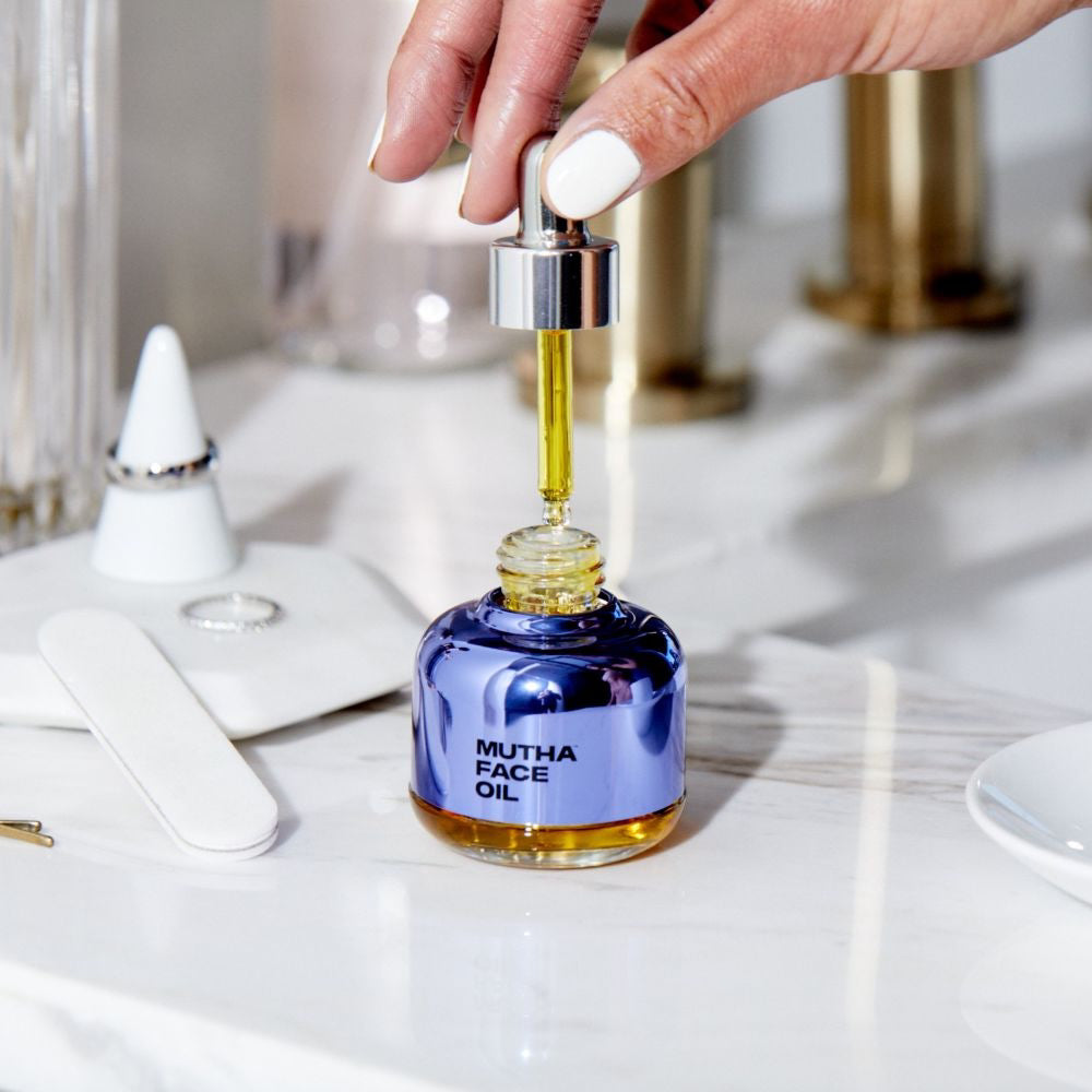 Image of the Face Oil on a filled marble countertop with a hand holding up the dropper of the Face Oil