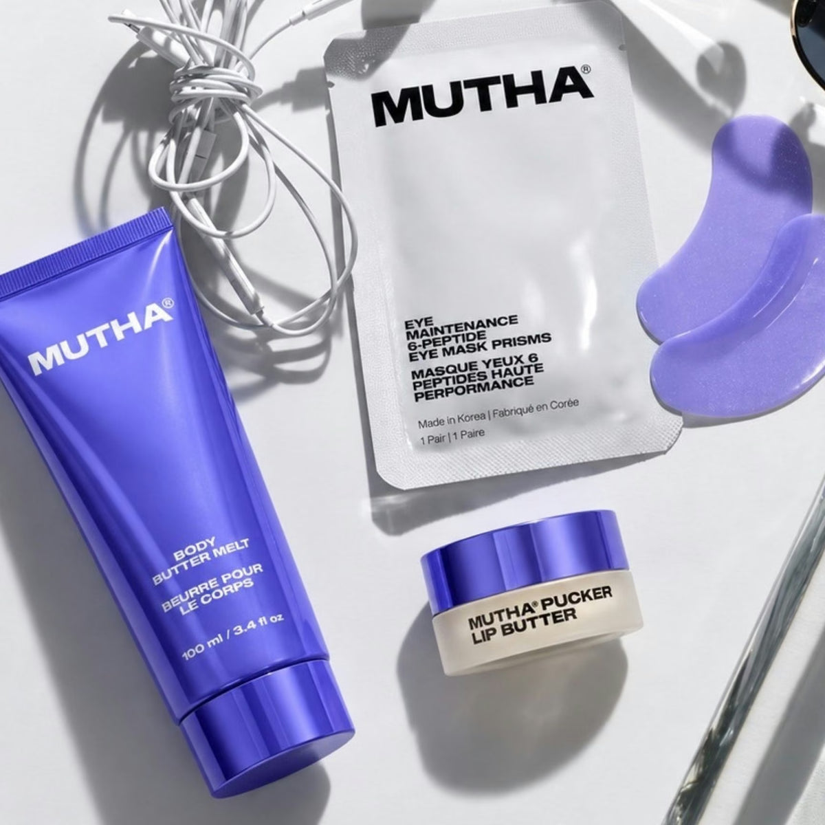 Body Butter Melt, Eye Mask Prisms and Pucker Lip Butter flat-laid with earphones.