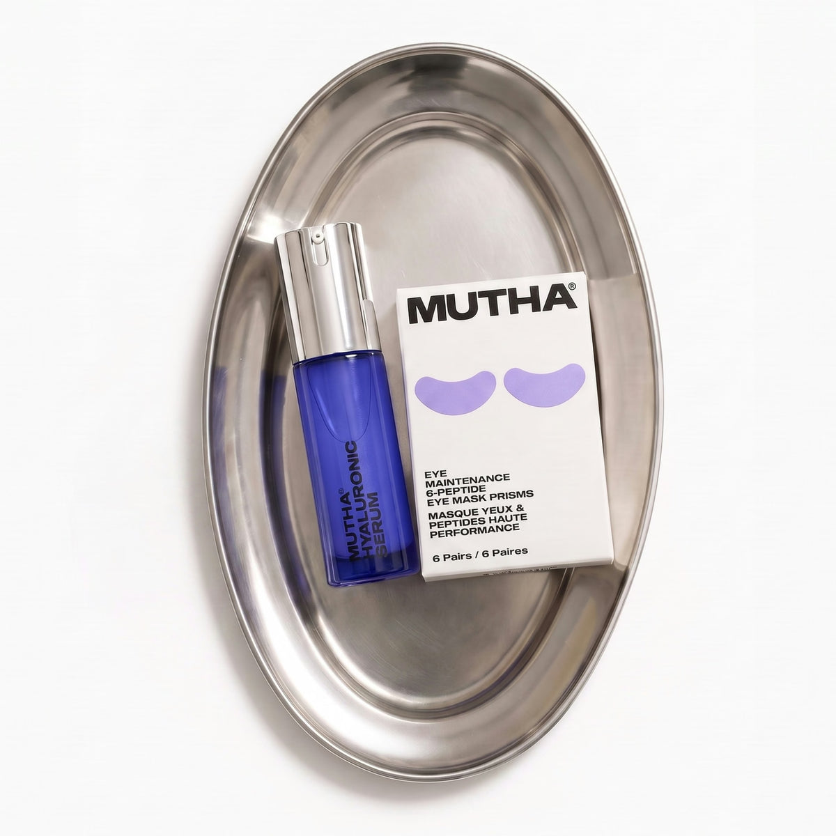 The Hyaluronic Serum and Eye Mask Prisms box arranged on a brushed steel oval tray, shot from above