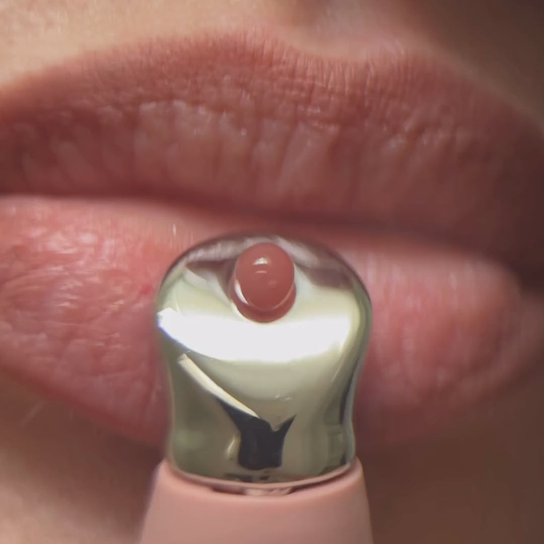 Macro footage of Pucker Up Lip Plump being applied with the metal applicator, leaving lips full and high-shine