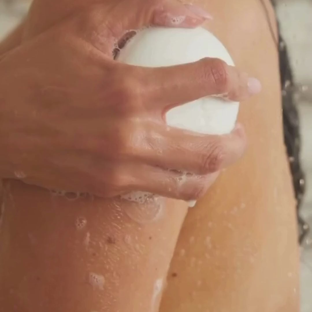 A model lathers the white Dirty Citrus body bar over wet skin in the shower, building a rich foam