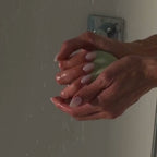 A model rinses the green Detox Greens body bar under running water in the shower