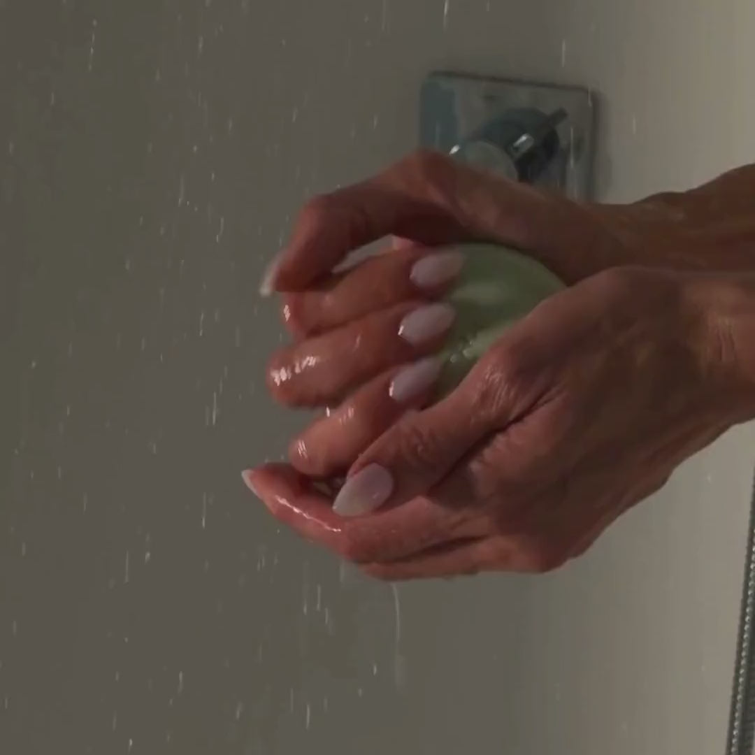 A model rinses the green Detox Greens body bar under running water in the shower