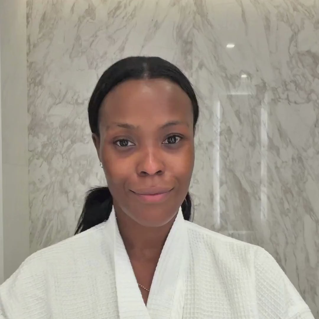 A model in a robe applies the purple Eye Mask Prisms under each eye in a marble bathroom