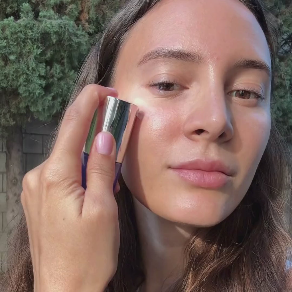 A model applies MUTHA Hyaluronic Serum to her face in natural daylight, pressing it under the eyes and across the cheeks