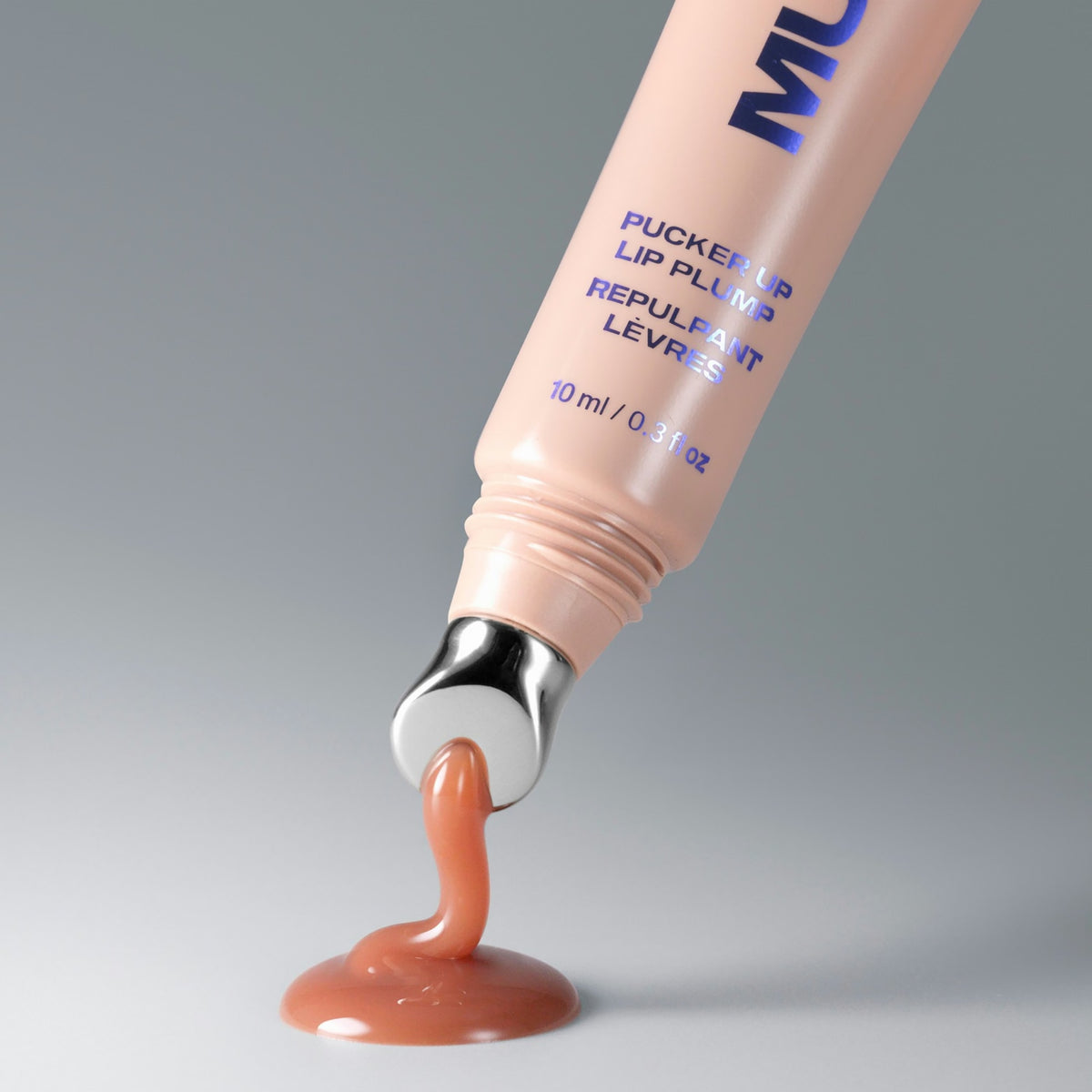 Macro shot of the Pucker Up Lip Plump metal applicator dispensing a drop of warm nude-brown gloss